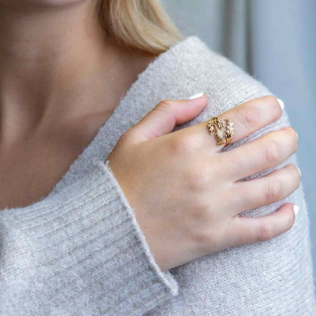 Bronzen ring met distelbloem aan een wijsvinger van een rechterhand die leunt op de linkerschouder.