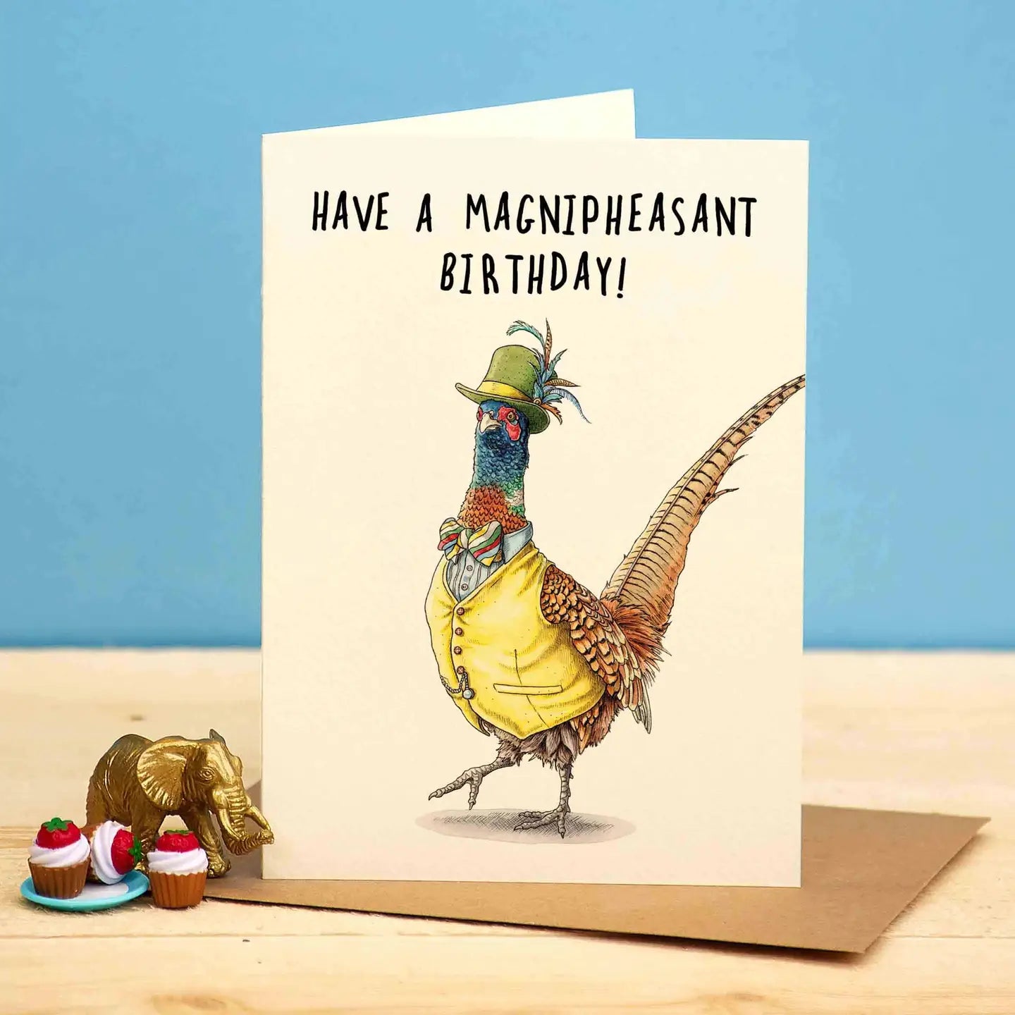 Verjaardagskaart met een chique geklede fazant die een gevederde hoed, hemd met strik en gilet draagt. Daarboven staat de tekst "Have a Magnipheasant Birthday"